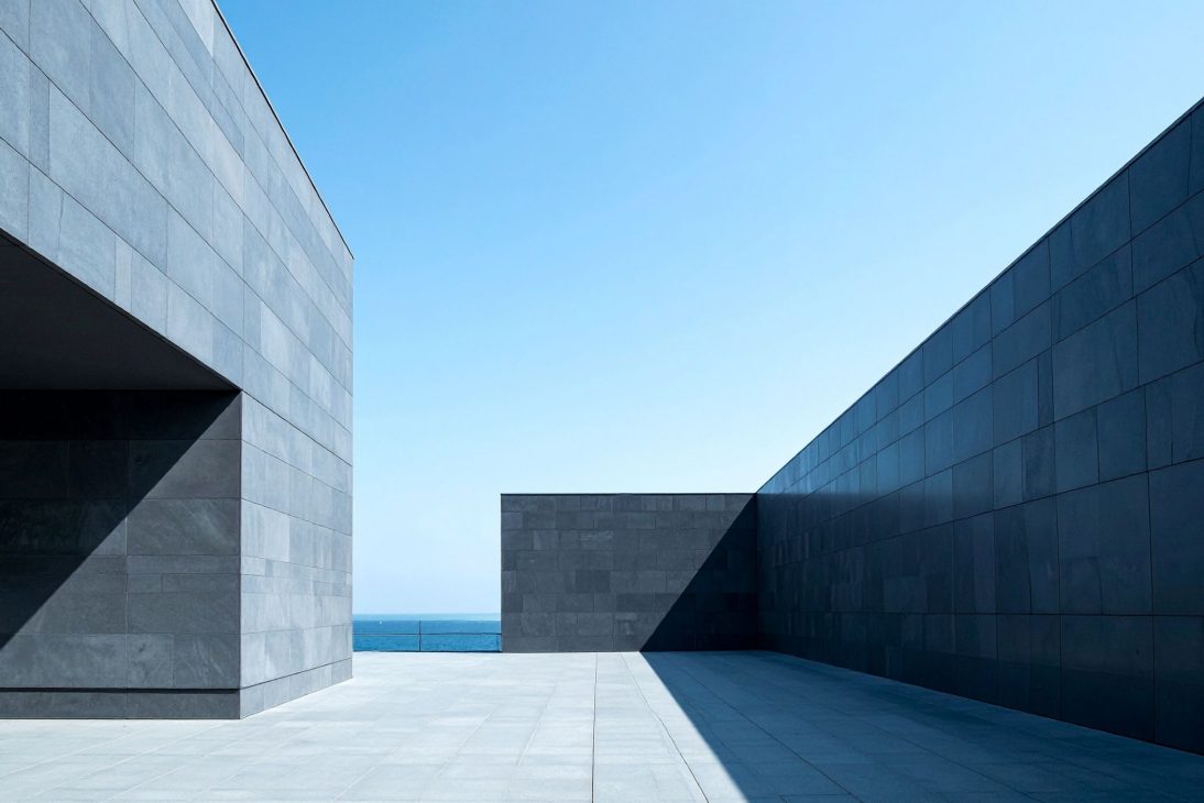 Arquitetura moderna com paredes cinzas e céu azul ao fundo, estilo minimalista, junto ao mar.