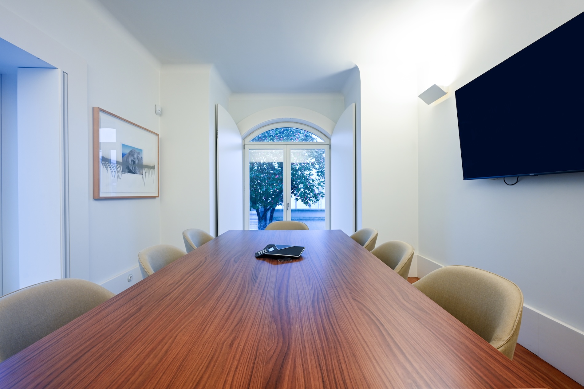 Sala de reunião moderna com mesa de madeira, cadeiras confortáveis e janela com vista para árvores.