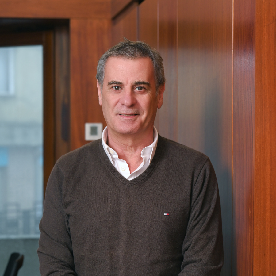 Man in a brown sweater standing indoors with wooden panel background.