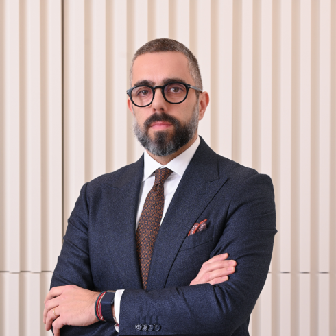 Homem de óculos e fato formal, braços cruzados, contra fundo com parede texturizada verticalmente.