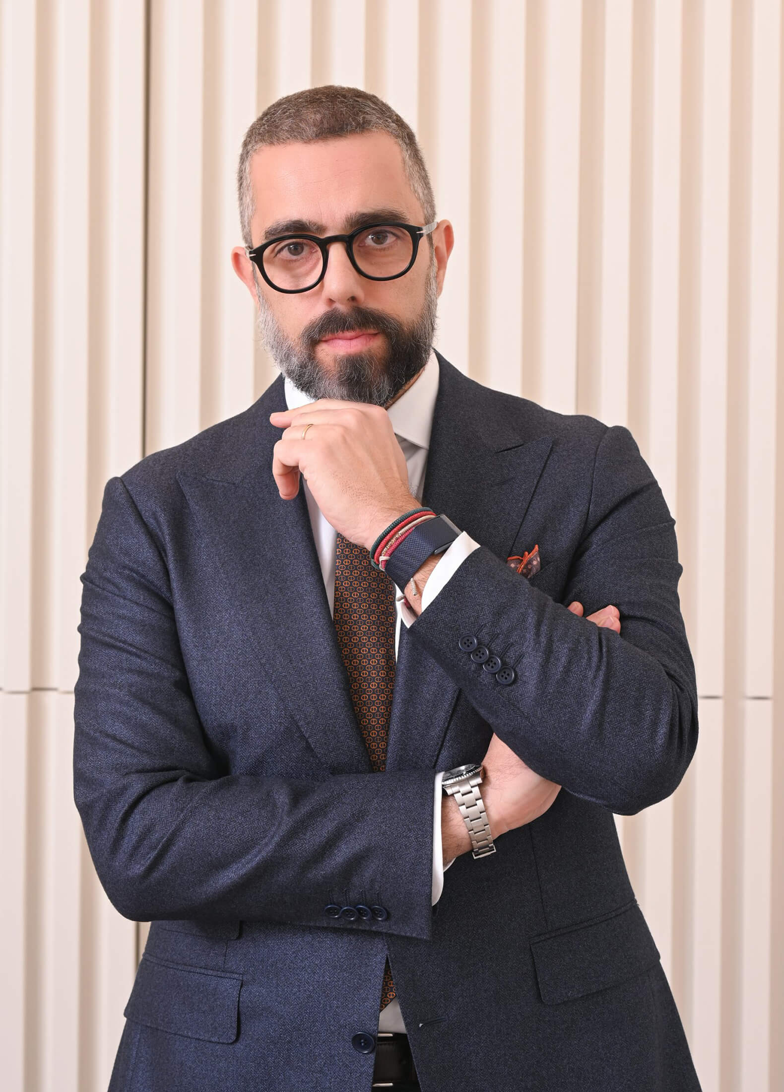 Homem de negócios confiante em fato azul com óculos, mão no queixo, fundo de parede com textura.